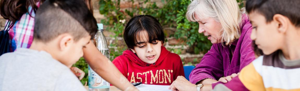 geflüchtete Kinder lesen mit Seniorin in einem Buch