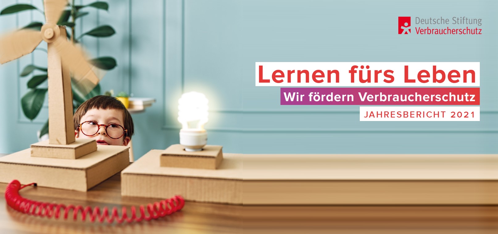 iStok.com/ pinstock kleiner Junge mit Brille beobachtet gespannt Windkraftanlage aus Papier und Glühbirne