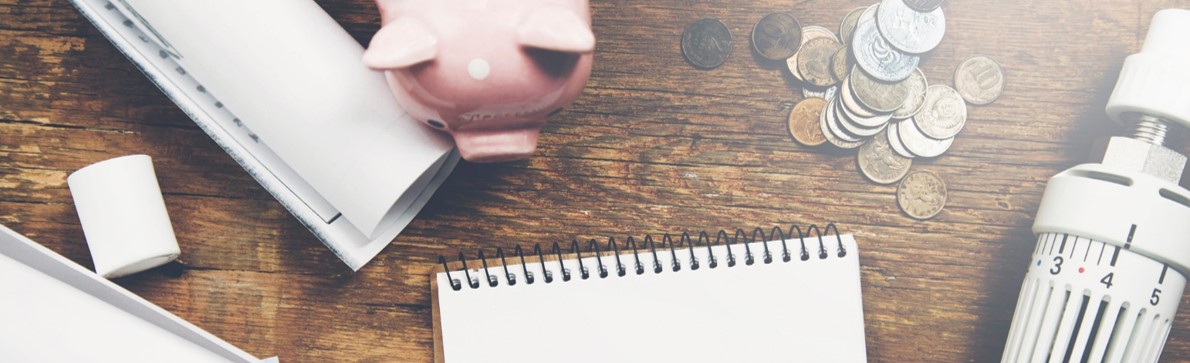 iStock.com/Aramyan Schreibtisch mit Heizregeler und Sparschwein